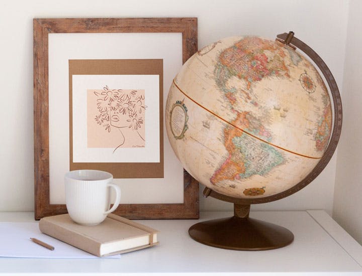A coffee cup on a white table sourounded by a globe and a framed piece of Lisa's art